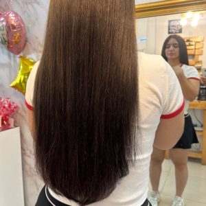 A bundle of straight, silky Color 2 hair extensions displayed on a mannequin head in front of a mirror. The rich brunette shade is smooth and glossy.