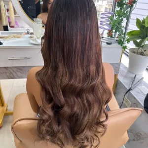High-quality Color 4 hair extensions in a warm brown shade, styled straight with a natural shine, displayed in a salon setting with a mirror and greenery.