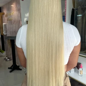 Color 60 blonde hair extensions – A close-up image of silky, straight, platinum blonde (Color 60) hair extensions displayed on a stand with a mirror in the background.