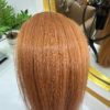 Copper hair extensions displayed on a mannequin head in a salon setting, showcasing the smooth texture and vibrant color. A mirror and hair bundles are visible in the background.