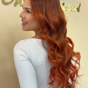 Copper hair extensions displayed on a mannequin head in a salon setting, showcasing the smooth texture and vibrant color. A mirror and hair bundles are visible in the background.